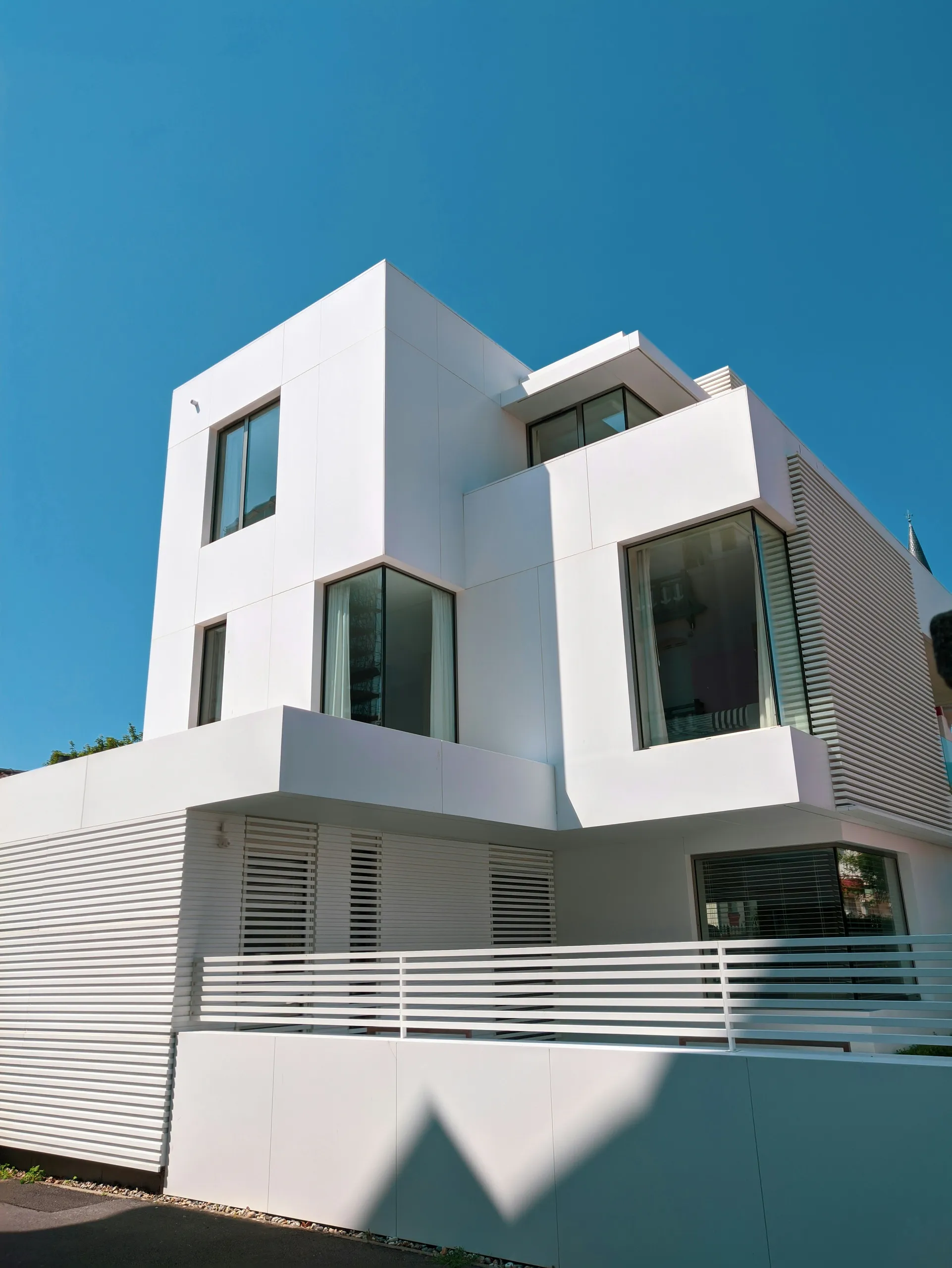 Casa blanca moderna de volumen geométrico y grandes cristaleras sobre un cielo azul
