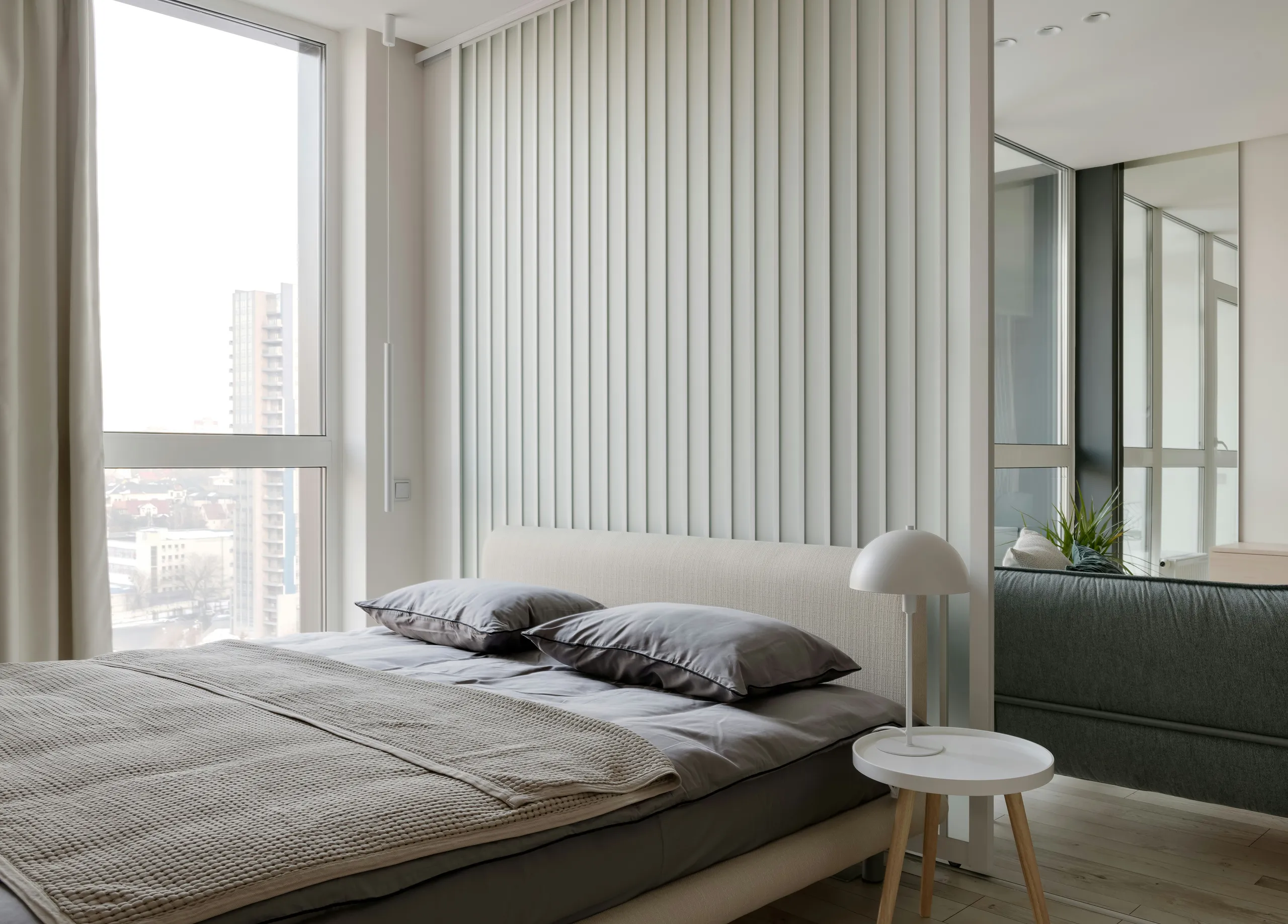 Dormitorio luminoso y minimalista con ventanal panorámico, ropa de cama gris y vistas a la ciudad